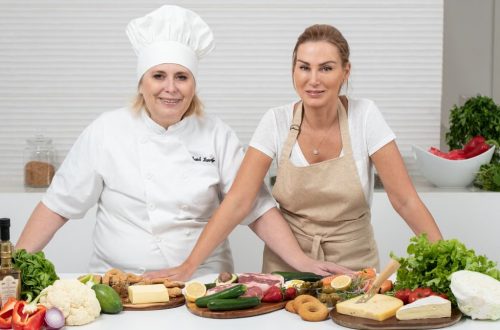 Two female chefs with variety of fresh ingredients in a kitchen setting, showcasing culinary preparation.