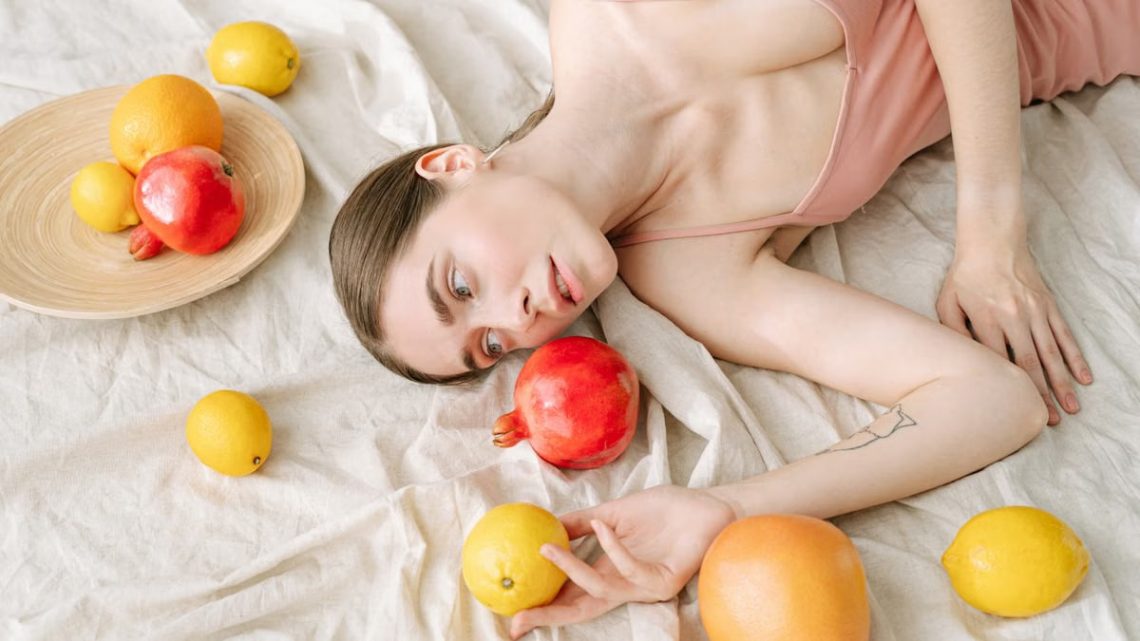 A serene woman in pink lies among vibrant citrus fruits on a soft linen cloth.