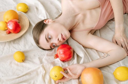 A serene woman in pink lies among vibrant citrus fruits on a soft linen cloth.
