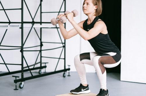 A woman in sportswear performs a squat with dumbbells indoors, embodying strength and healthy living.